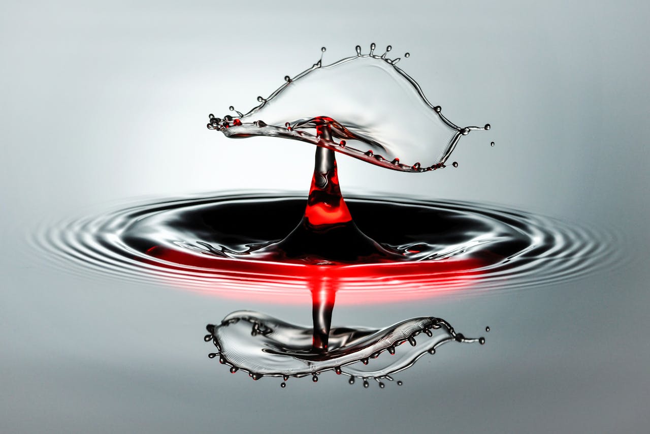 Stunning macro shot capturing a water drop collision with vibrant red hues creating a unique artistic form.
